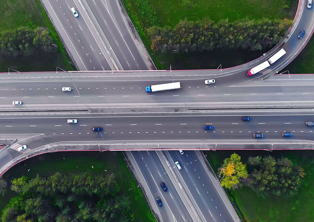 Aerial view of busy multi-lane highway with moving cars and trucks, capturing fast-flowing urban traffic from above.