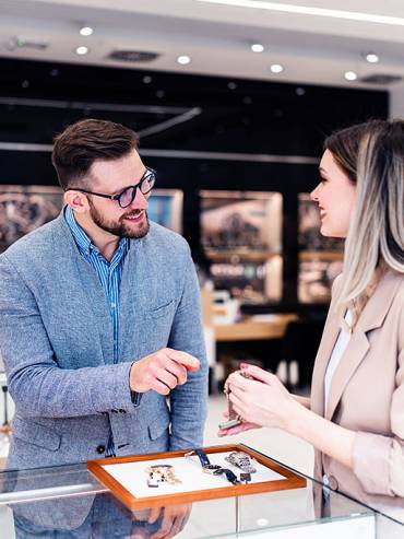 Man and woman in business attire examining a watch inside a stylish, well-lit watch shop with elegant interior design.