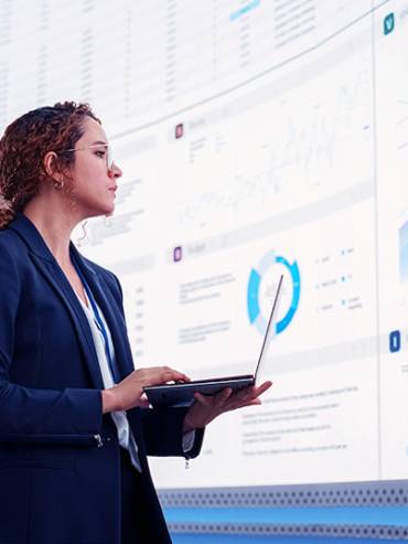 Confident woman in business suit standing while holding a laptop, showcasing professionalism and readiness.
