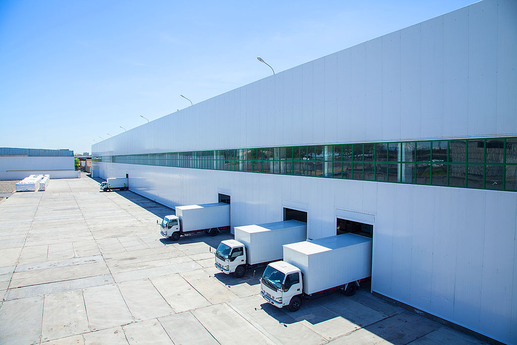 Large warehouse with multiple trucks parked outside, illustrating a busy logistics hub with active vehicle staging.