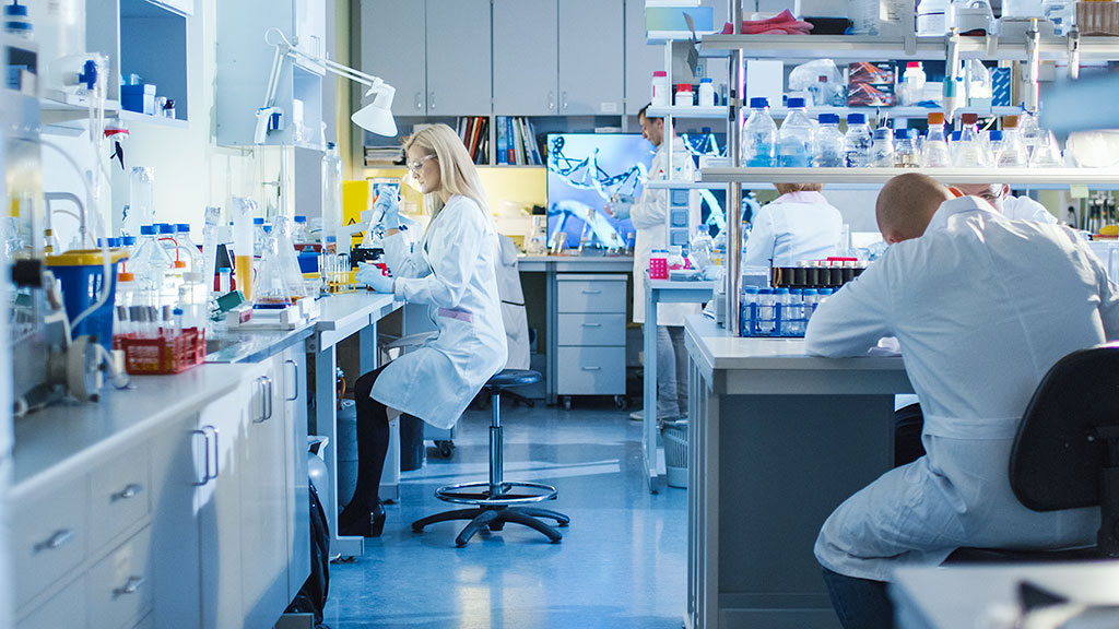 Bright modern laboratory with scientists in white coats using microscopes and lab equipment, featuring organized benches and data displays.