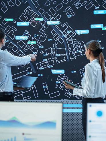 Two people examining a map on a computer screen, discussing and planning their route collaboratively in an indoor setting.