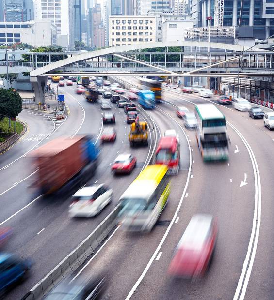 hong-kong-busy-highway-traffic High-angle view of busy Hong Kong highway with blurred fast-moving vehicles, curved lanes, pedestrian bridge, and urban buildings.
